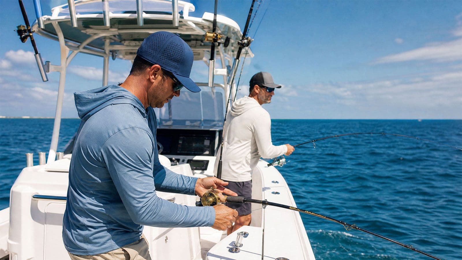 Two men wearing performance hats fishing from a center-console boat on the open ocean.