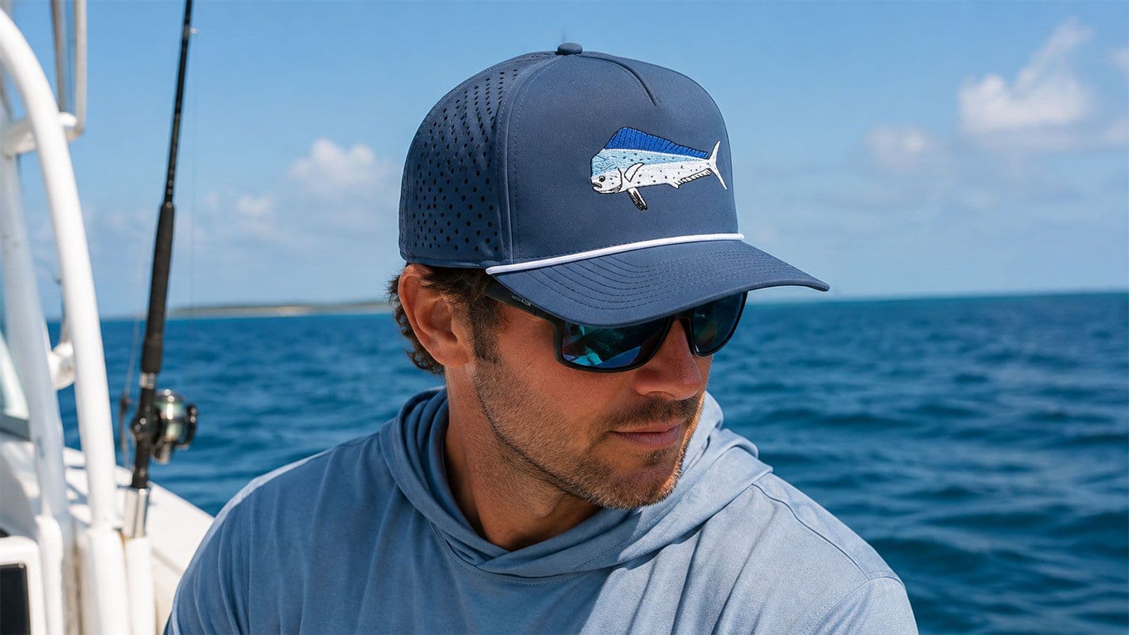 Man wearing a navy performance fishing hat with a mahi design while boating offshore.