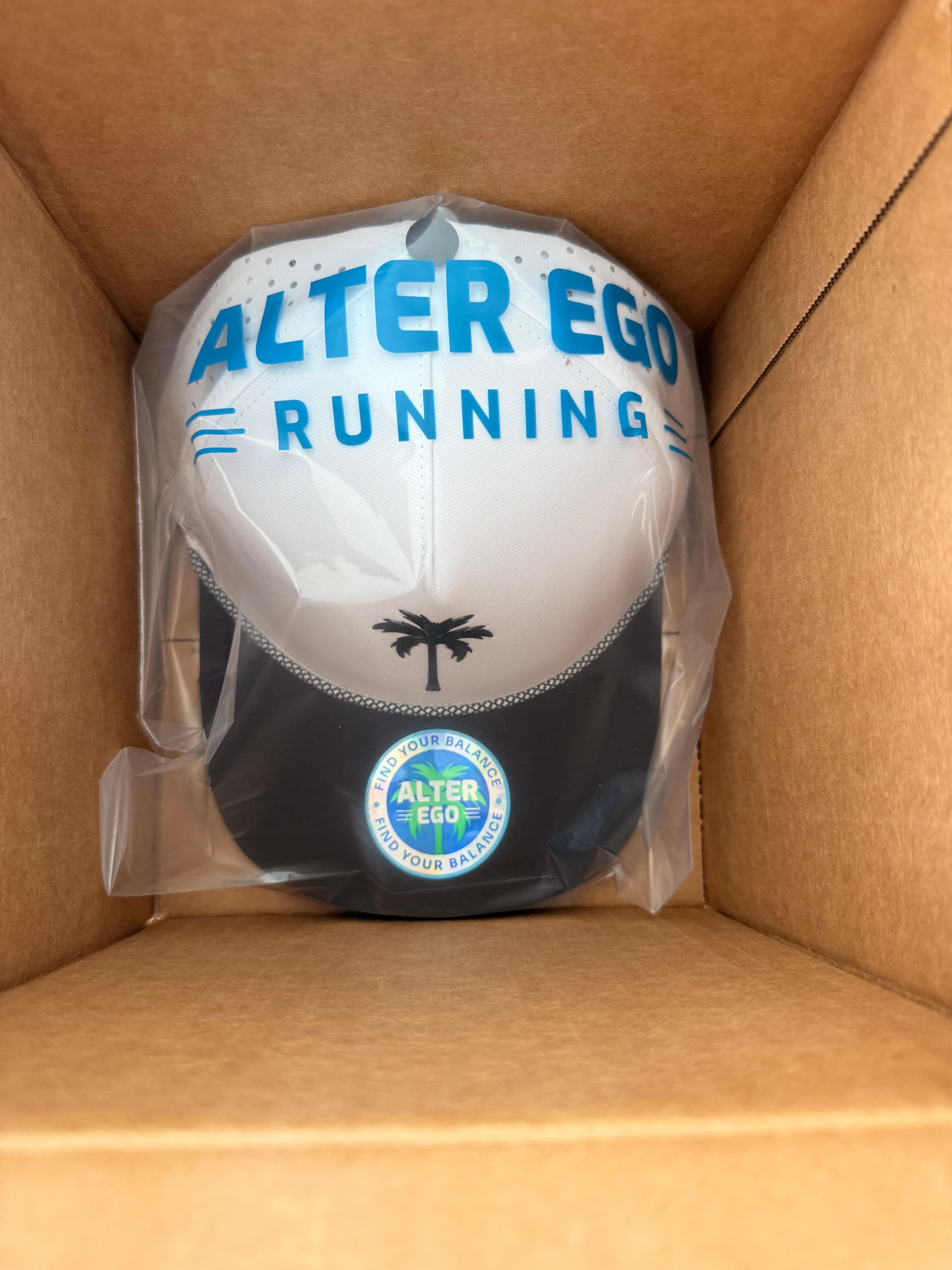 The Alter Ego Coaster Splash Classic Black White Palm hat, still wrapped, lifted out of its shipping box